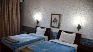 Een kamer met twee bedden, elk met een blauwe spreidek en witte kussens, een ingelijst schilderij aan de muur en een gestructureerde witte muur.