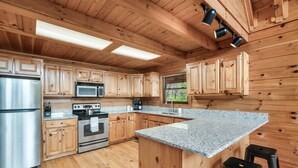 A kitchen with wooden cabinets, stainless steel appliances, granite countertops, and a central island with stools.