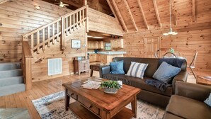 A spacious loft-style room with a wooden interior, a staircase, a kitchen area, and a cozy seating area with a sofa and chairs.