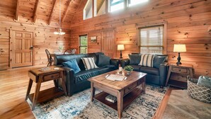 A cozy log cabin interior with a wooden ceiling, two sofas, a coffee table, and a rug.