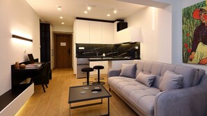A modern living room with a grey sofa, a black coffee table, and a kitchen area with white cabinets and black countertops. - Superior Suite | Zotos Luxury Living #2 (Thessaloniki)