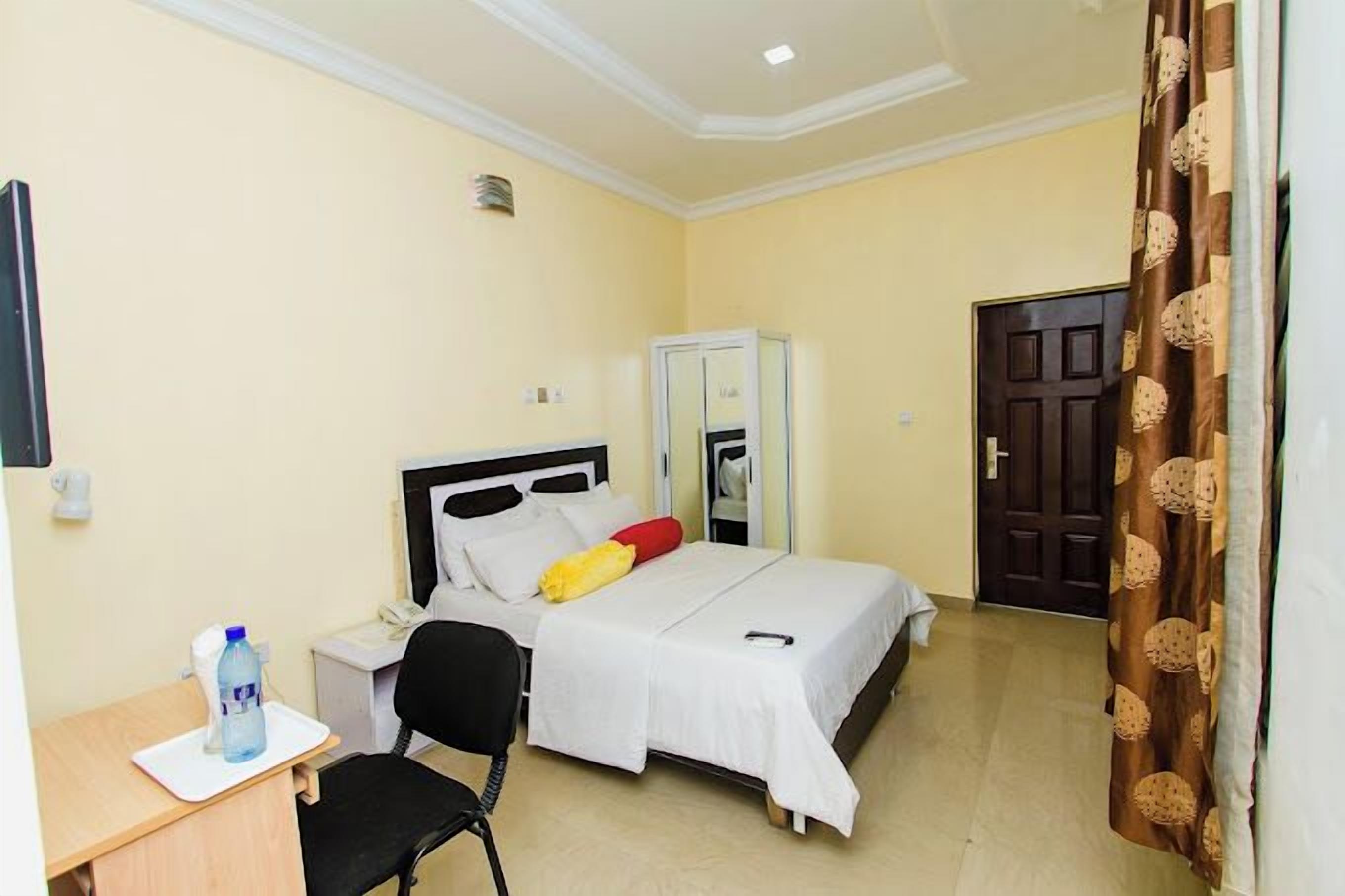 Una habitación de hotel con una cama, un escritorio con silla, un armario y una puerta.