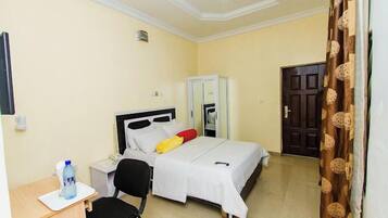 Una habitación de hotel con una cama, un escritorio con silla, un armario y una puerta.