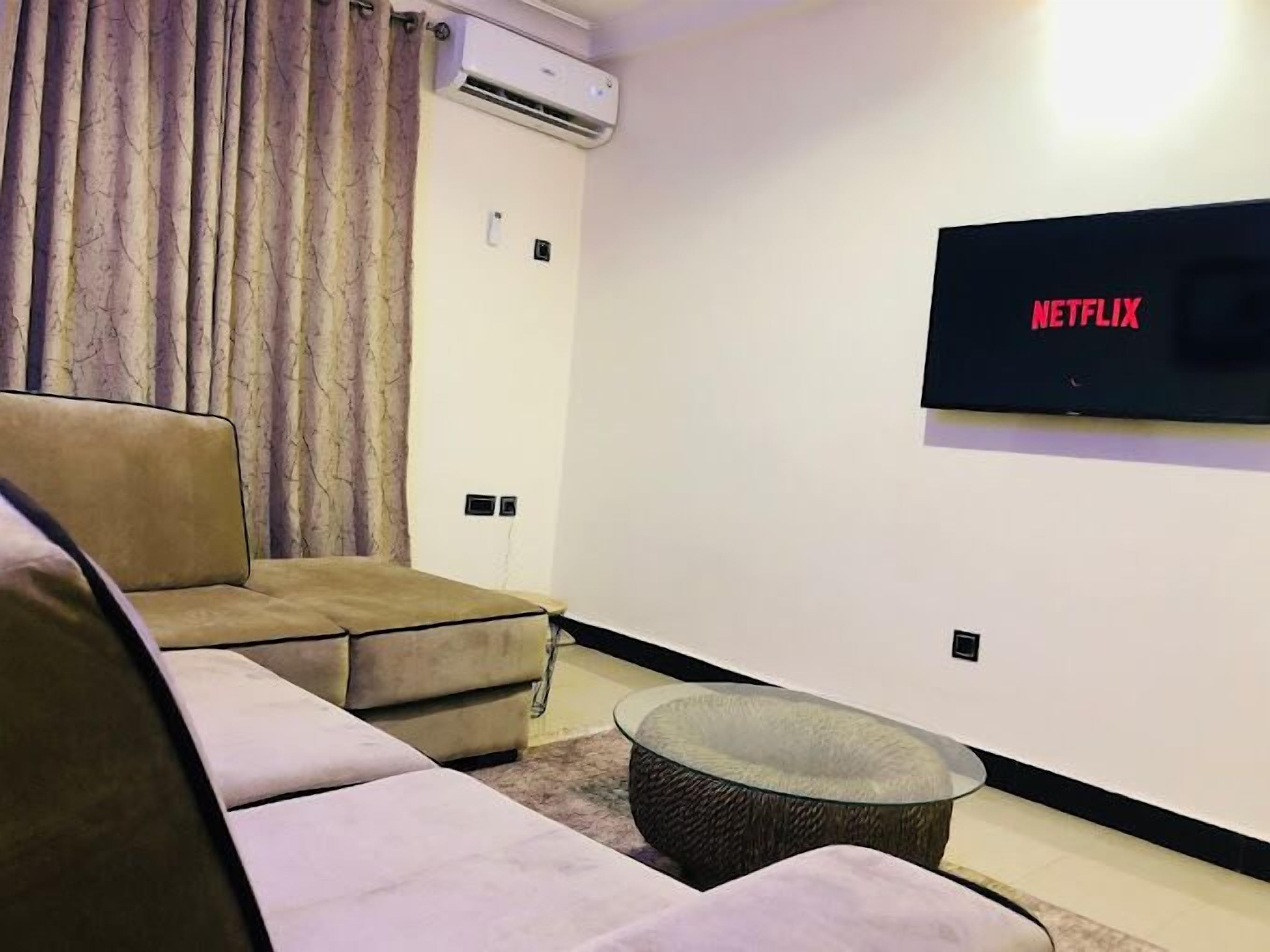 A modern living room with a beige sofa, a glass coffee table, and a flat-screen TV mounted on the wall.