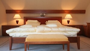 Een groot bed met een houten hoofdbord, twee bedlampen en een schipdecoratie erboven.