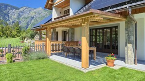 Een huis met twee verdiepingen, een overdekte patio, zonnepanelen en uitzicht op de bergen.