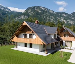 Chalet-style building with a gabled roof, nestled among lush greenery and mountains.