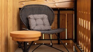 A wooden cabin with a sloped ceiling, a wicker chair with a cushion, and a small wooden table.