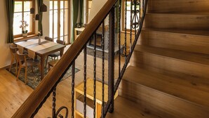 A wooden staircase with a wrought iron railing leading to a room with a dining area and large windows.