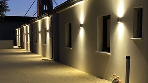 A building with a series of illuminated windows and a gravel driveway. - Comfortable gîte ideally located (Saint-Martin-d'Ardèche)