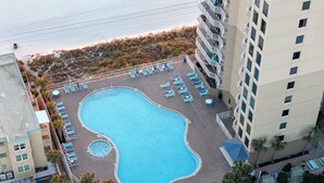Vista aerea di un hotel con una grande piscina circondata da lettini prendisole e una piccola vasca idromassaggio.