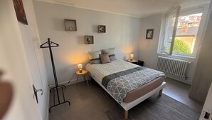 A bedroom with a bed, bedside lamps, a radiator, and a window with a view. - Air-conditioned accommodation downtown Rodez  (Rodez)
