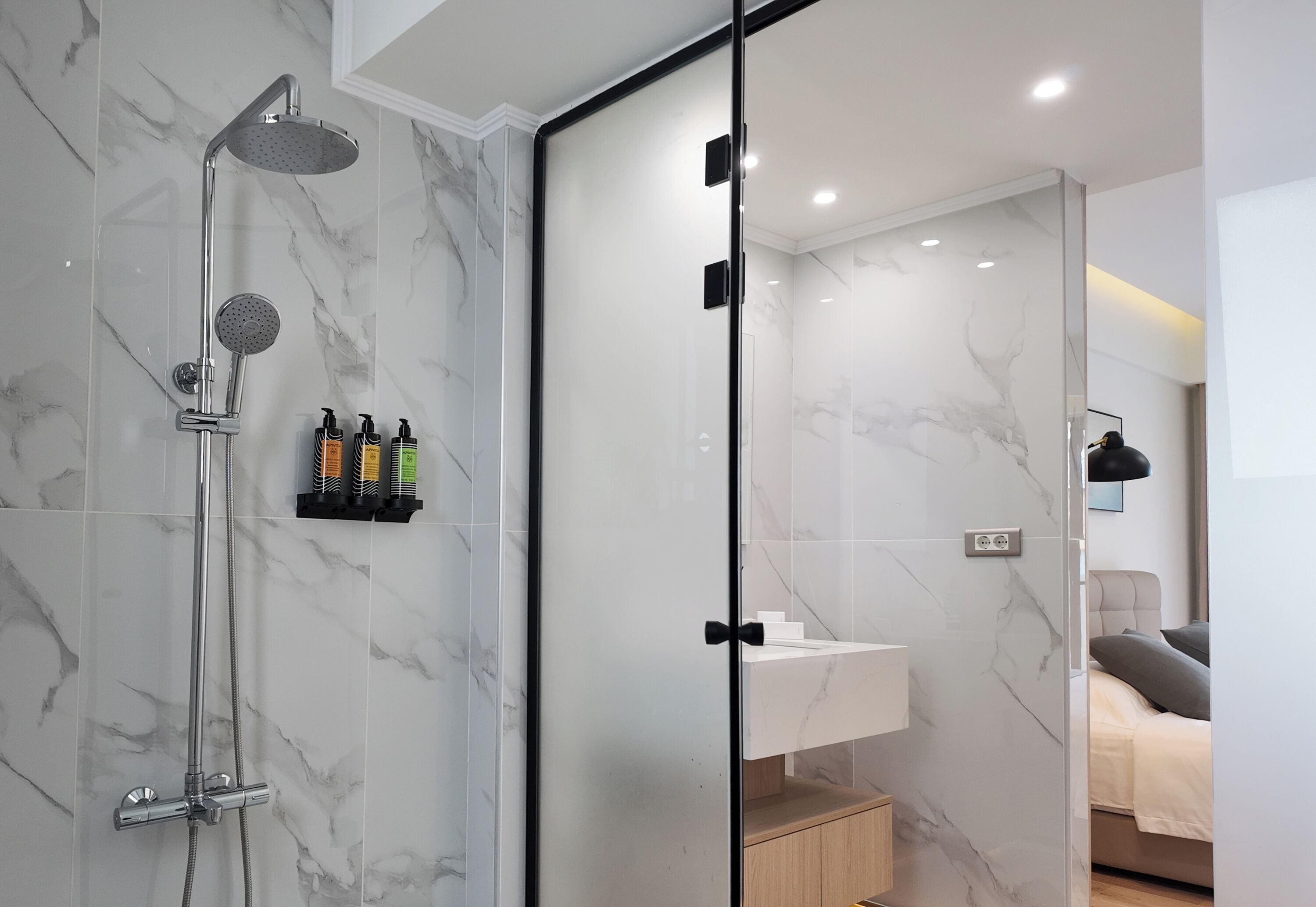 A modern bathroom with a glass shower enclosure, marble walls, and a visible sink area.
