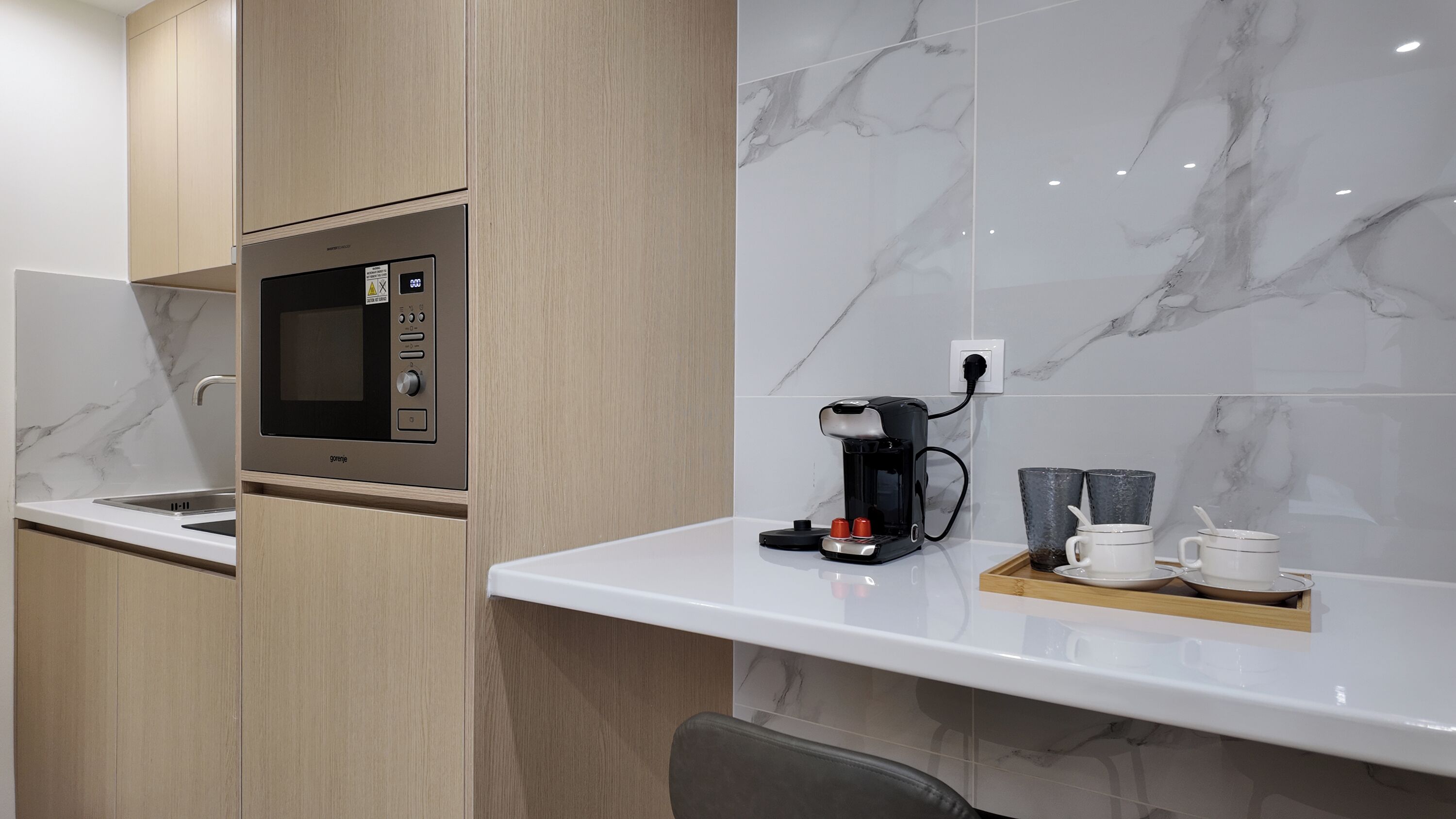 A modern kitchen with a built-in microwave, coffee maker, and a tray with cups and a teapot.