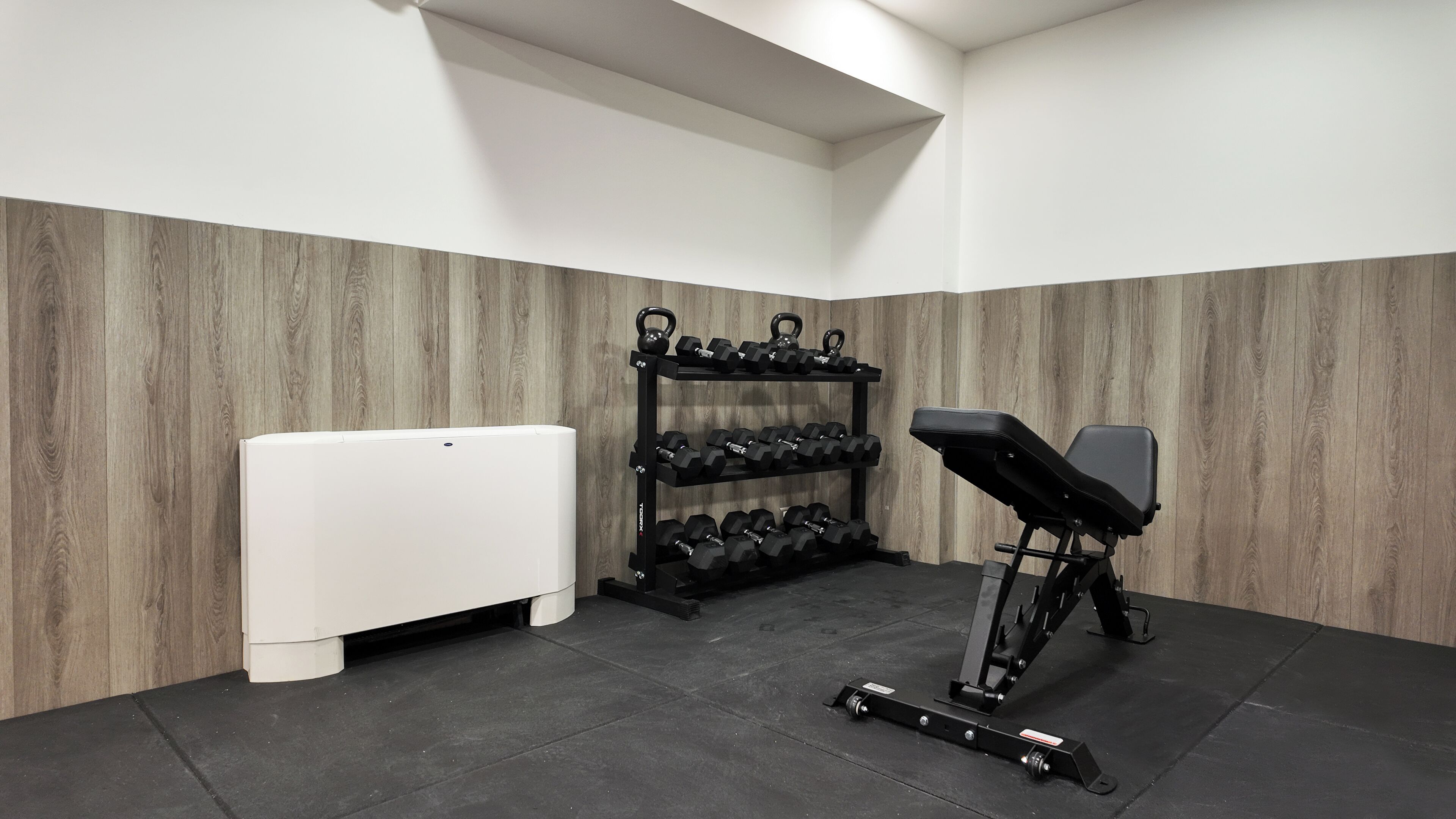 Ein Fitnessraum mit Hantelgestell, Kurzhanteln, einer Trainingsbank und Laufband.