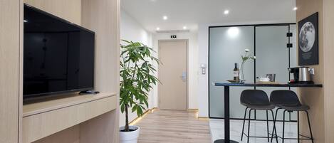 Una habitación de hotel moderna con una televisión de pantalla plana, una planta en maceta, una mesita con una botella de vino y copas, dos sillas negras y una gran fotografía enmarcada de la luna en la pared.