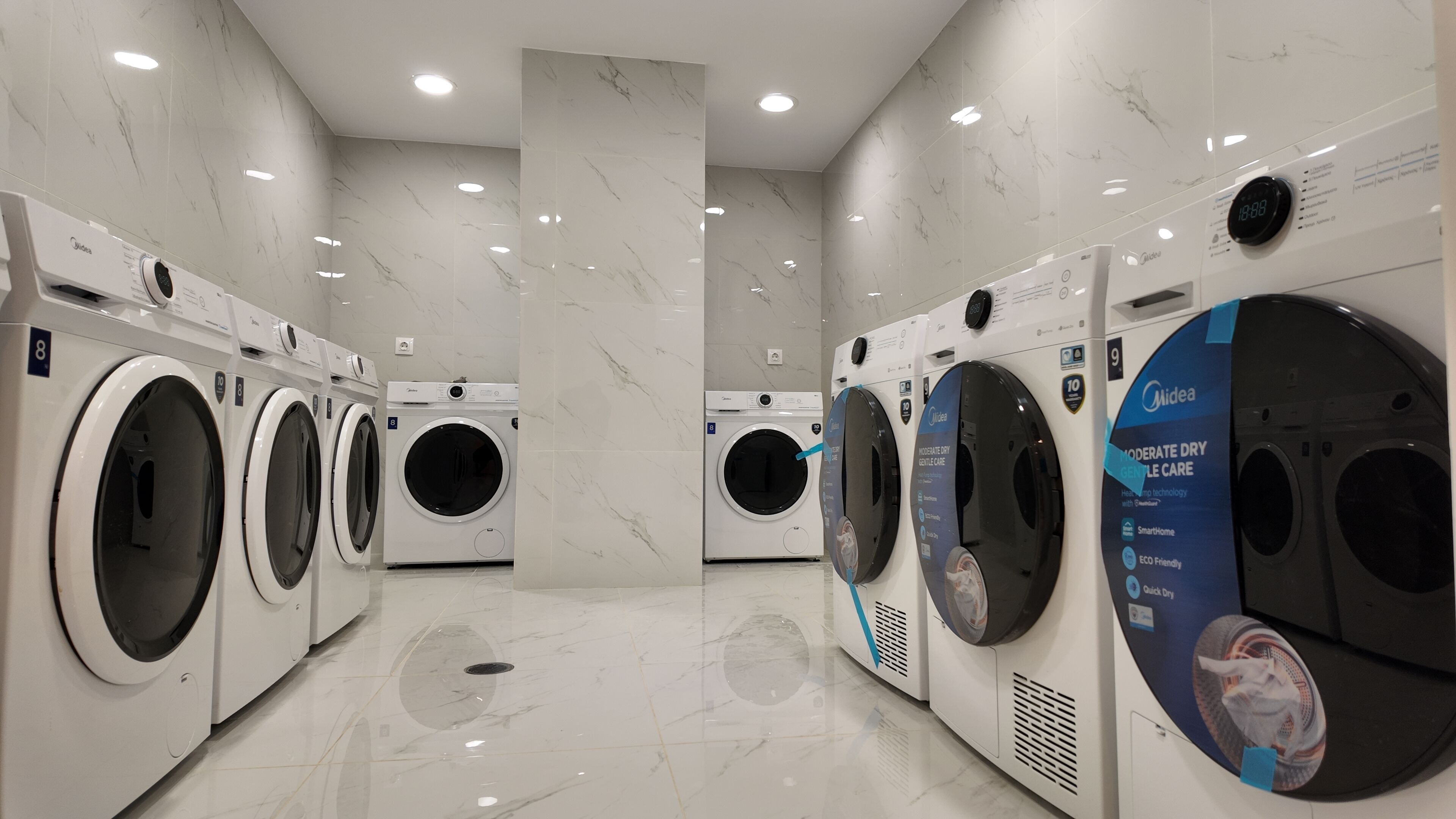 A modern laundry facility with multiple washing machines, marble flooring, and recessed ceiling lights.