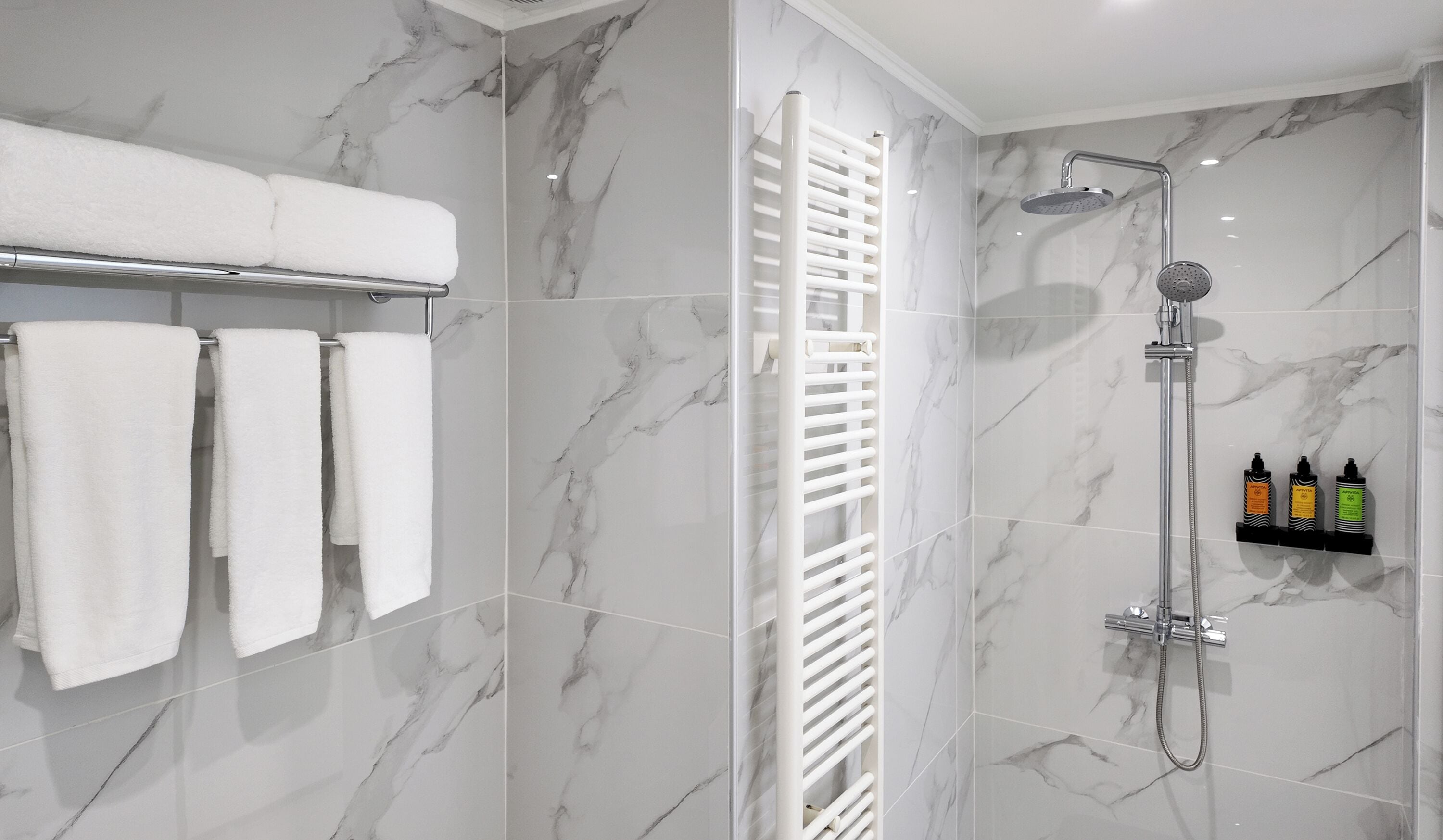 Un baño moderno con paredes de mármol, un perchero blanco, un box de ducha de vidrio y un estante con artículos de aseo.