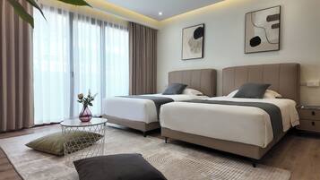 A modern hotel room with two beds, a small round table with a vase, and a view of the city through large windows.