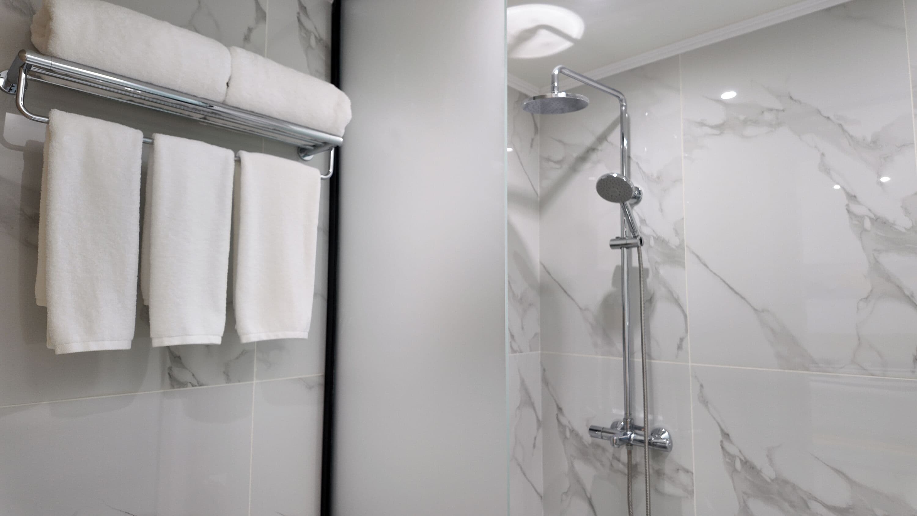 Un bagno moderno con box doccia in vetro, un portasciugamani con tre asciugamani e pareti in marmo.