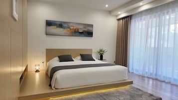 A modern bedroom with a large bed, a painting above it, and a view through sheer curtains.