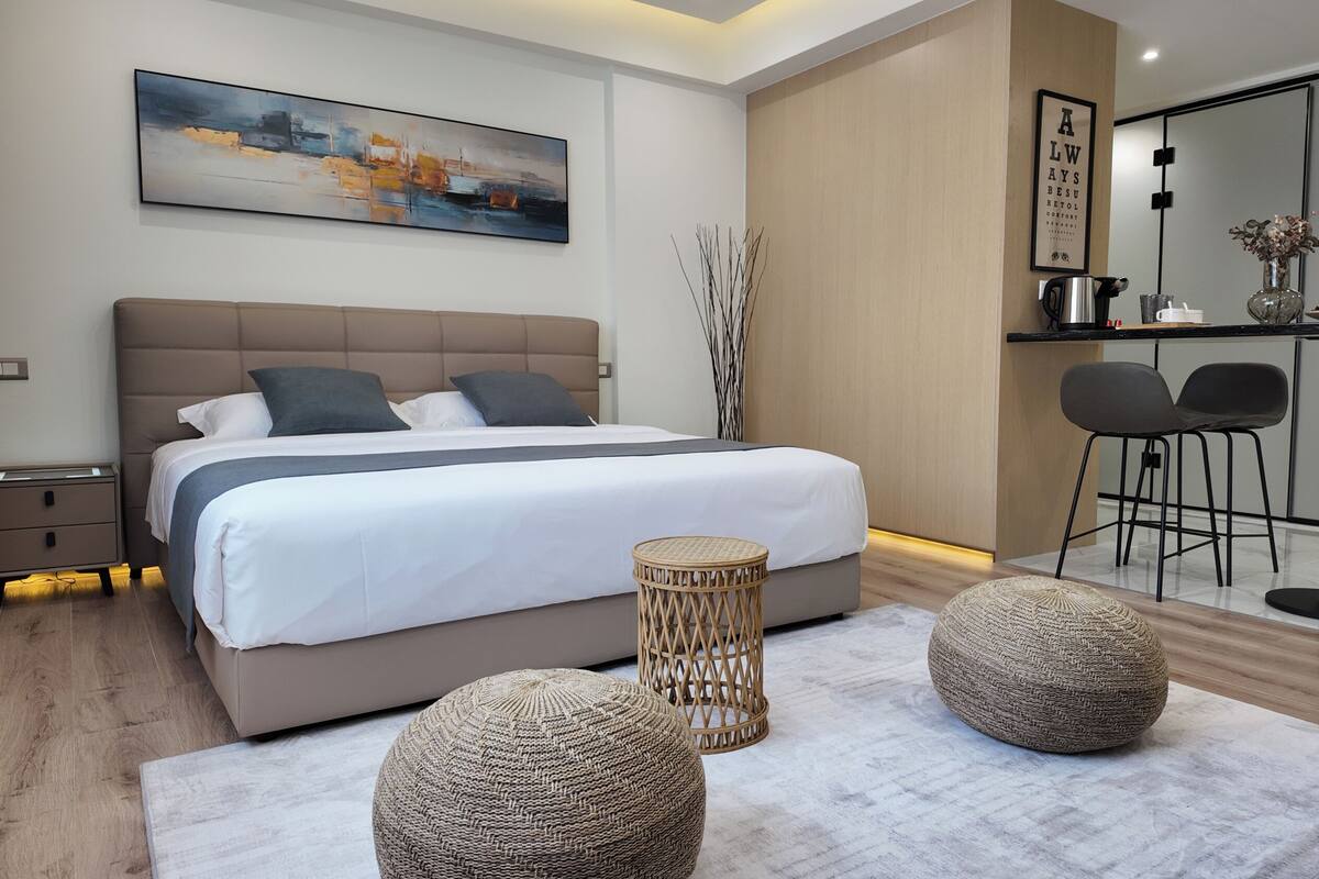 Un dormitorio moderno con una cama grande, mesitas de noche, una pequeña mesa con sillas y un cuadro en la pared.