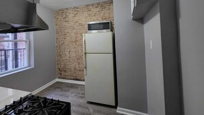 Una cocina compacta con pared de ladrillo, un refrigerador y una estufa a gas.