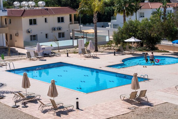 Un área de piscina con dos piscinas separadas, sillas de descanso y sombrillas.