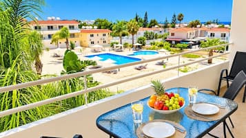 Un balcón con una mesa lista para comer, con vistas a una piscina y una zona residencial.
