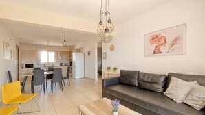 A modern living room with a sofa, a coffee table, and a dining area with chairs and a table. - Narcissos Nissi Beach Apartment D12 (Ayia Napa)