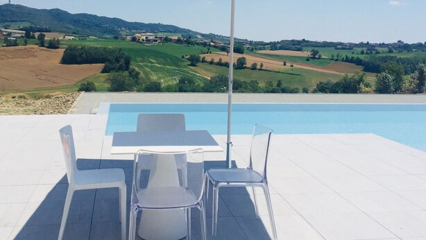 Ein Poolbereich mit Tisch und Stühlen, umgeben von großen Sonnenschirmen, mit Blick auf eine malerische Landschaft und einen Pool.
