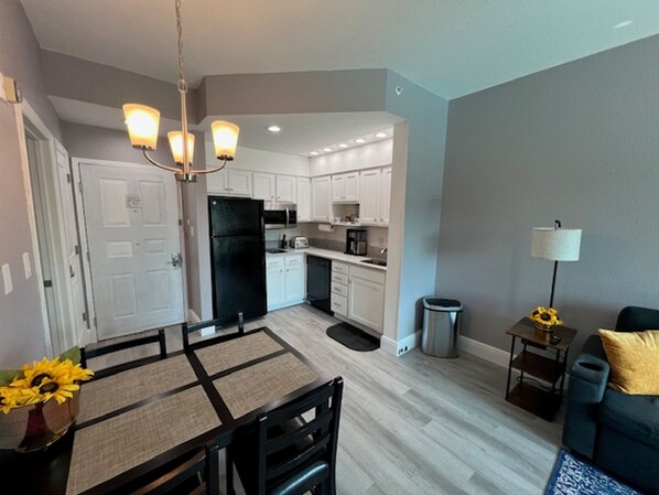 A modern kitchen with white cabinets, a black refrigerator, and a dining area with a table and chairs.