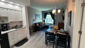 A modern kitchen with white cabinets, a dining area with a table and chairs, a sofa, and a chandelier. - Univeral Disney Epic Shuttle (Orlando)
