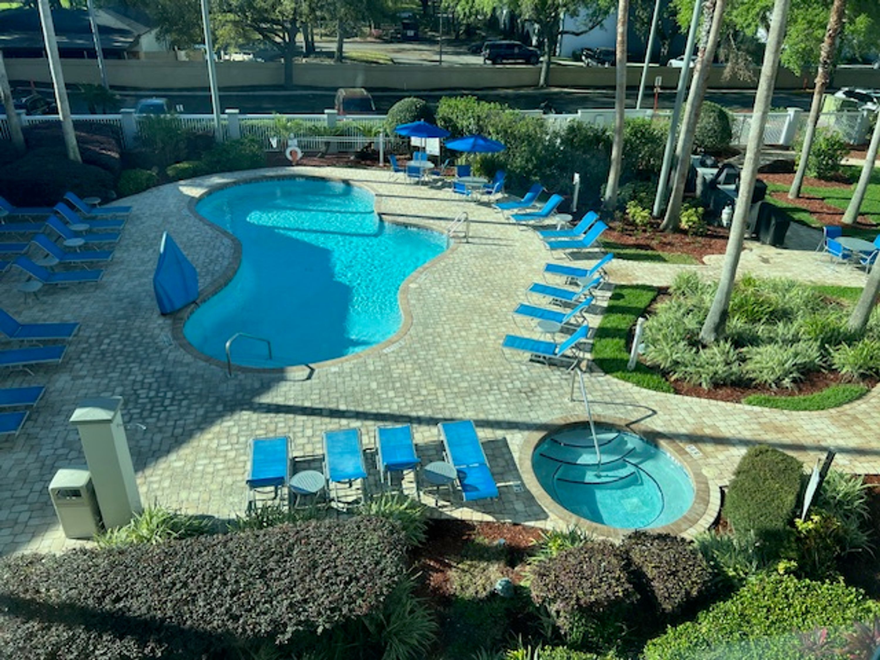 A pool area with multiple lounge chairs and umbrellas, surrounded by landscaped gardens and a paved walkway.