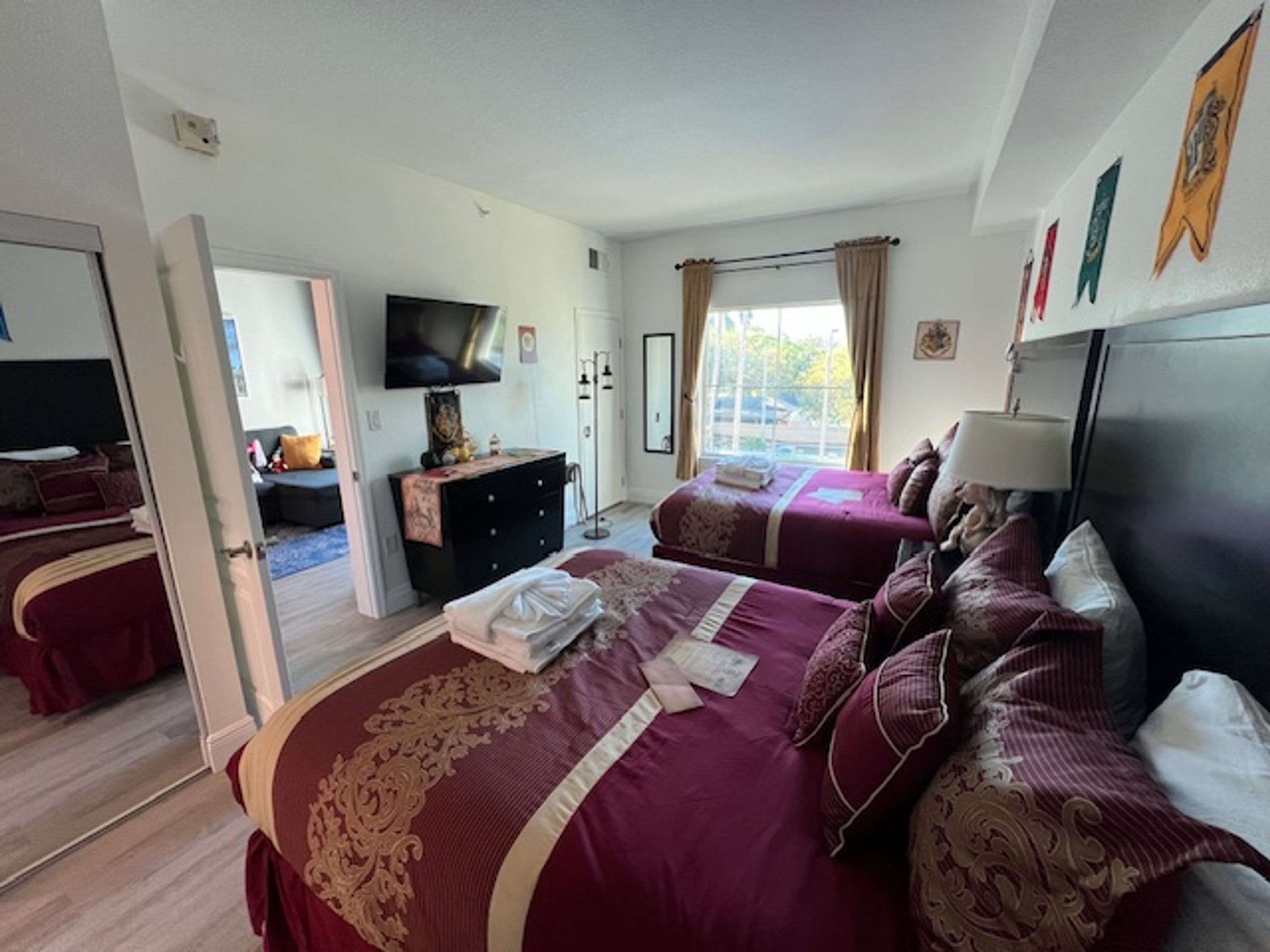 A hotel room with two beds, a TV, a dresser, and a window with curtains.
