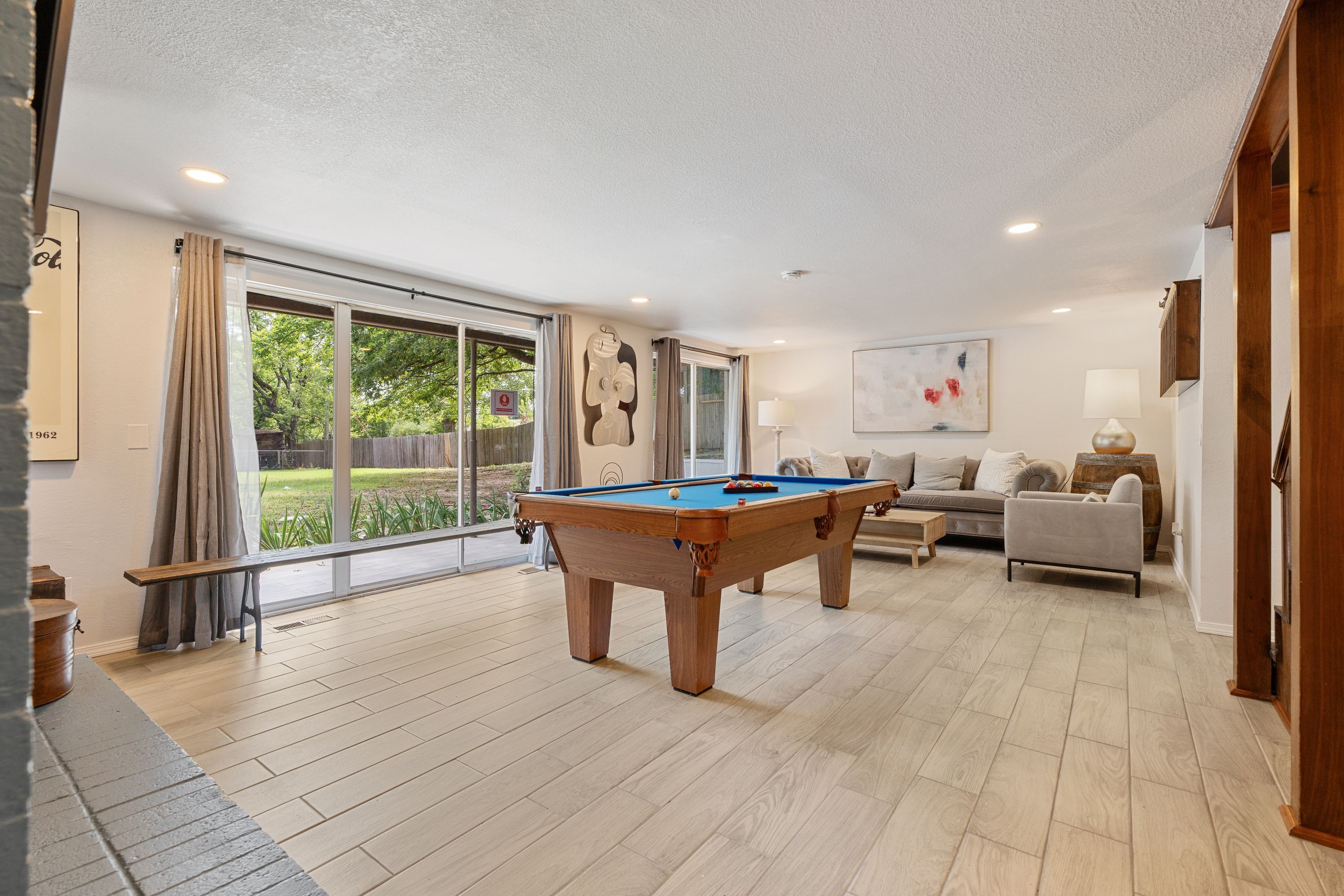 A spacious living area with a pool table, a sofa, and a large window offering a view of the outdoors.