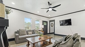 Ein Wohnzimmer mit grauem Sofa, einem Holztisch und einem Deckenventilator.