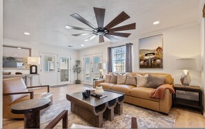 A spacious living room with a large ceiling fan, a leather sofa, a coffee table, and a dining area with a table and chairs. - Spacious Lakefront View With Hot Tub and Pool NH (Oklahoma City)