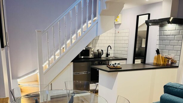Una cocina moderna con una mesa y sillas de vidrio, una escalera y un sofá azul.