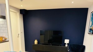 Una sala de estar moderna con una pared de acento azul oscuro, un mueble de entretenimiento negro, un sofá azul y piso de madera.