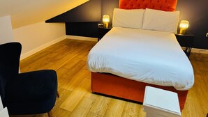 Un dormitorio moderno con cama, dos mesitas de noche, una silla y techo inclinado.