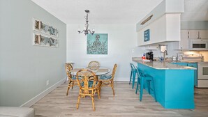 A modern kitchen with a turquoise island, white cabinets, and a dining area with wicker chairs. - Festival Sale! Beachside Paradise~2/1~Heated Pool (Gulf Shores)