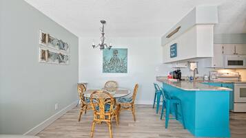 A modern kitchen with a turquoise island, white cabinets, and a dining area with wicker chairs.
