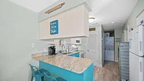 A kitchen with a marble countertop, turquoise bar stools, a coffee maker, a microwave, and a sign that says "Kindness Always in Style". - Festival Sale! Beachside Paradise~2/1~Heated Pool (Gulf Shores)