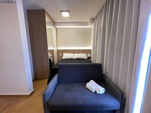 A hotel room with a bed, a seating area, and a nightstand. - ELEGANCE SUÍTES MAX JARDIM (São Paulo)