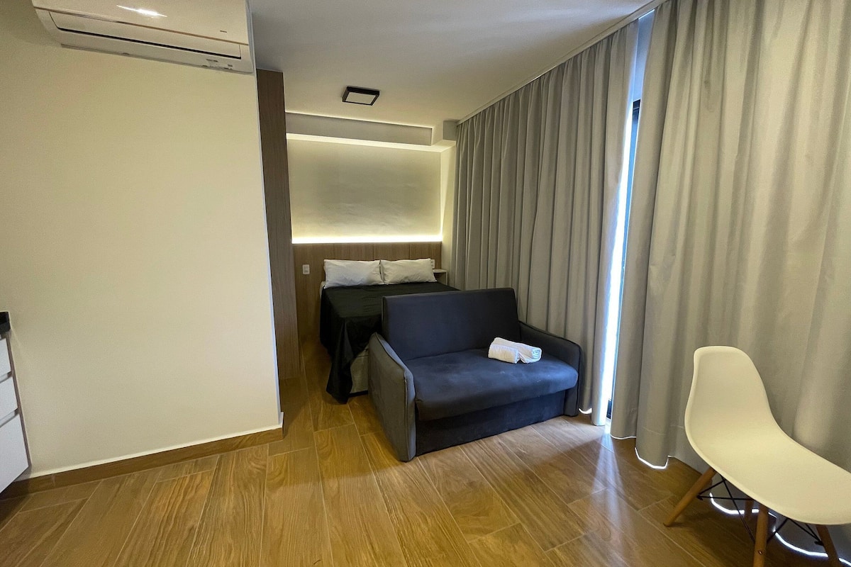 Una habitació d'hotel moderna amb un llit sofà, una cadira individual, televisió de pantalla plana i una finestra gran amb cortines.