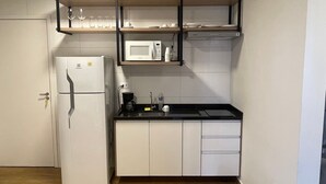 Ett kompakt kök med ett vitt kylskåp, en mikrovågsugn och en kaffebryggare på bänkskivan.