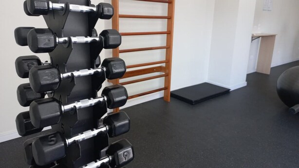 Ett gym med ett hantelställ som är fäst på väggen, en trästege och en svart matta på golvet.