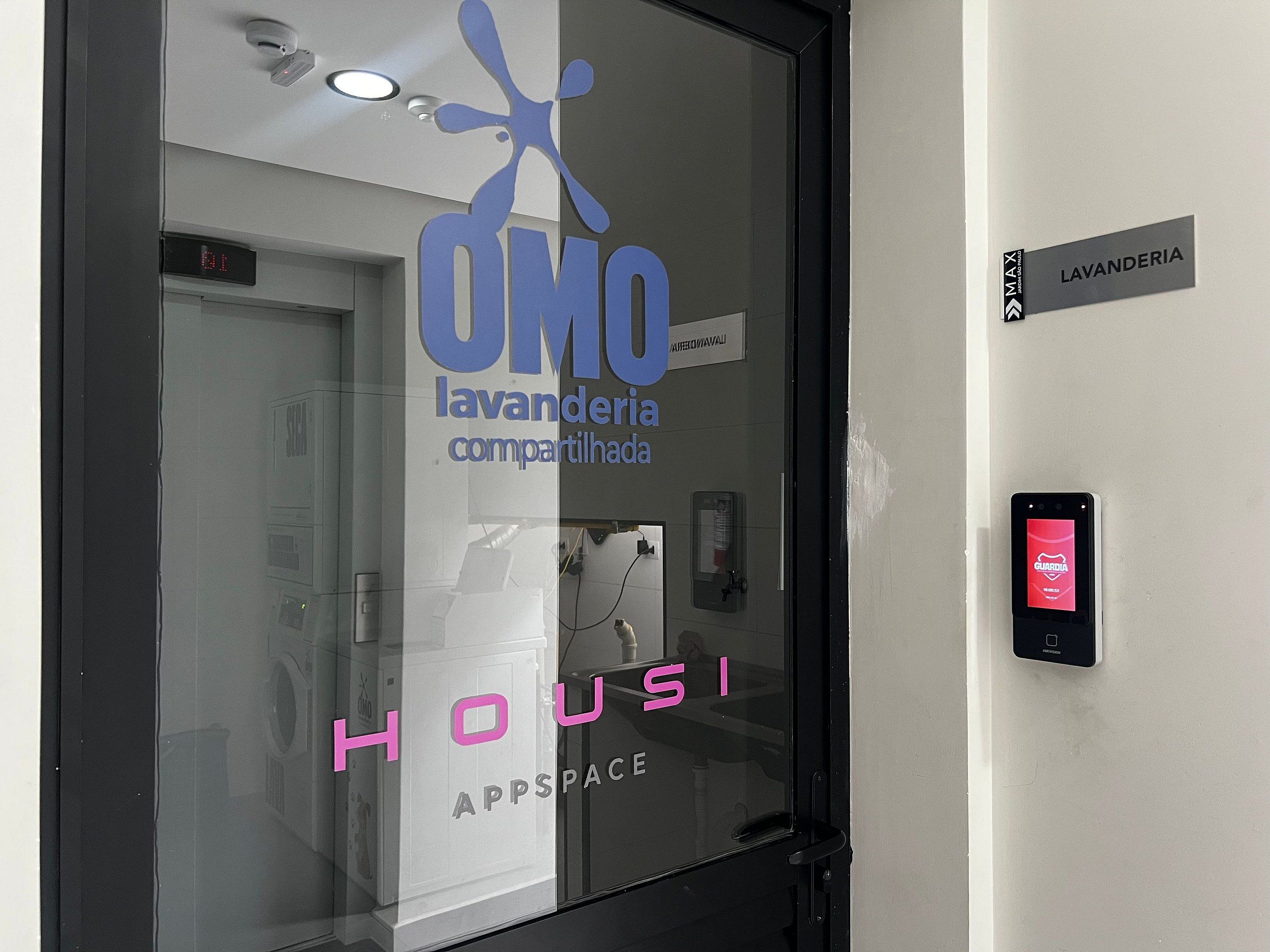 Ein Hotel Eingang mit einer Glastür, auf der das Logo "OMO" sowie die Schriftzüge "lavanderia compartilhada" und "HOU" zu sehen sind.