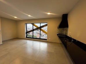 A spacious kitchen with a large window, a black range hood, and tiled flooring. - ELEGANCE SUÍTES MAX JARDIM (São Paulo)